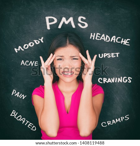 PMS premenstrual syndrome Asian woman holding head in pain having headache, stomach cramps, acne, mood swings with symptoms written on blackboard background in chalk. Royalty-Free Stock Photo #1408119488