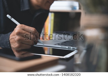 Online working, E learning, business and technology concept. Businessman using digital pen working on digital tablet and laptop computer in office. Man searching internet, using tablet pc on desk