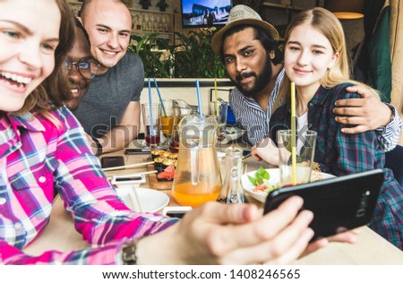 Group of young cheerful friends are sitting in a cafe, eating, drinking drinks. Friends take selfies and take pictures.