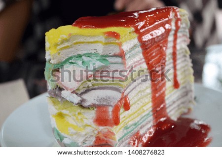 Closeup picture of colorful crepe cake with different vivid layers covered with velvet red syrup and creamy texture