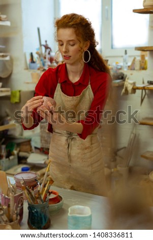 Organizing studio. Pleasant attractive woman checking her art pieces from clay while cleaning up working table