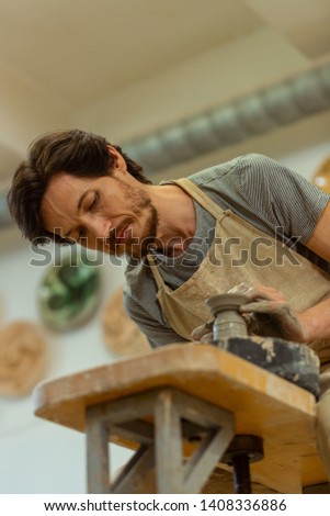 Professional wheel. Diligent dark-haired qualified master accurately creating pot while glancing on a process