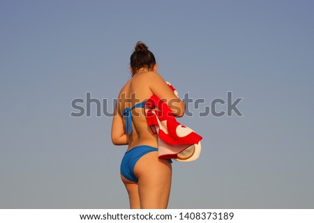 A girl in blue bikini with a red towel on the beach