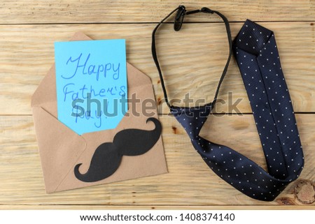 Happy father's day. text on a piece of paper in an envelope and a men's tie on a natural wooden background. top view