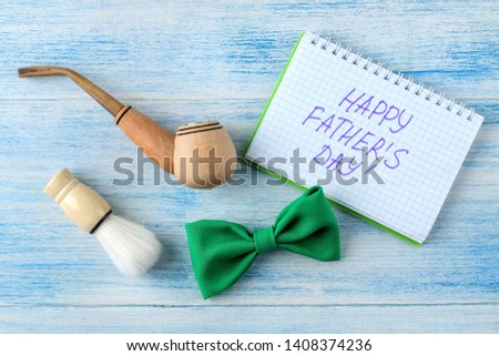 happy father's day. text and decorative men's tie butterfly and smoking pipe on a light blue wooden background. top view