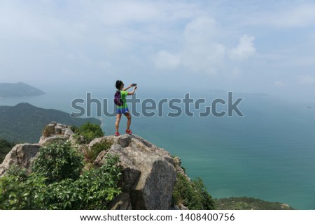 Successful Woman Hiker taking picture with smartphone In Seaside Mountain Top