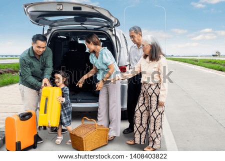Picture of three generation family preparing suitcase into a car for road trip while standing on the road