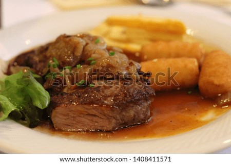 Picture of grilled meat with potatos with sauce and green sides on a white plate. Taken in a Restaurant in March 2019.