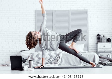 Young happy healthy fitness beautiful woman female doing vasisthasana yoga pose and workout on yoga mat opposite laptop with online master class at modern bedroom at home. Healthy lifestyle concept. Royalty-Free Stock Photo #1408415198