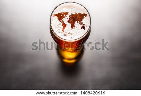 Global beer concept. World map silhouette on foam in beer glass on black table. Elements of this image furnished by NASA