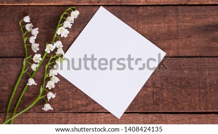 delicate white lilies of the valley on a brown wooden background with a sheet of white paper for text