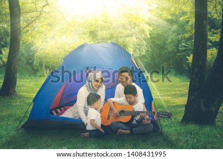 Picture of Muslim family singing and playing a guitar in a tent while camping in the forest at morning time
