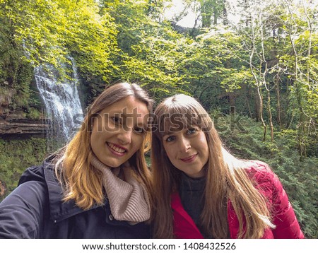 Two girls take selfies in front of a waterfall in Ireland