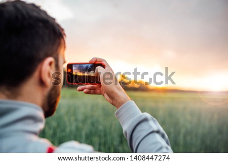 young man photographing sunset in nature with a smartphone camera