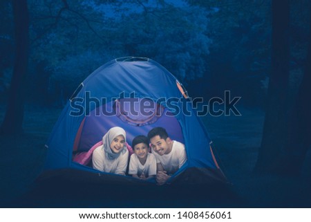 Picture of a happy Muslim family lying together in the tent while camping in the forest at night time