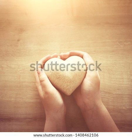 little child holding a wooden heart. father's and mother's day, love, hope and religion concept.