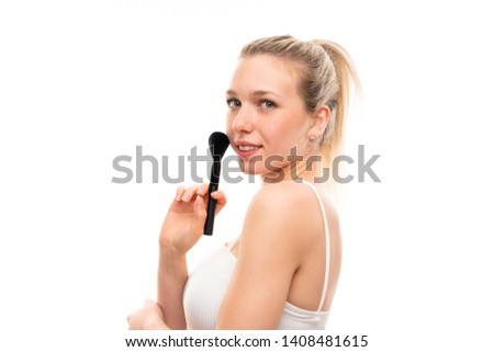 Young blonde woman over isolated white background with makeup brush