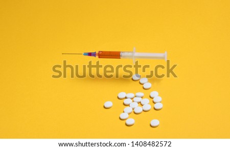 Medical minimalistic concept. Syringe, pills on yellow background.