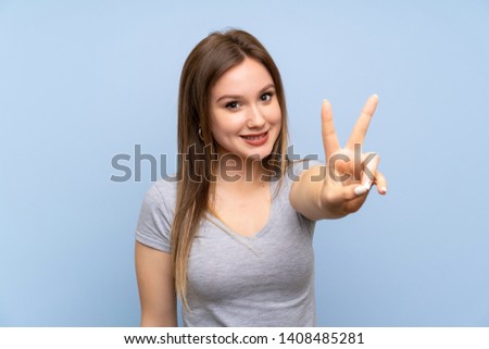 Teenager girl over isolated blue wall smiling and showing victory sign