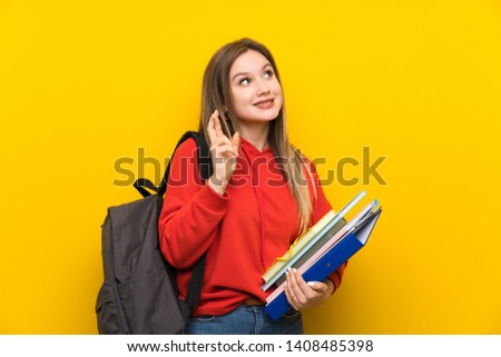 Teenager student girl over yellow background with fingers crossing
