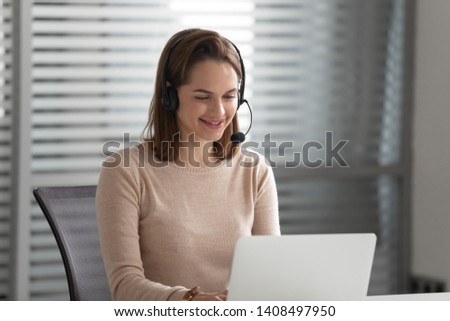 Smiling business woman customer support agent receptionist wear wireless headset video calling on computer looking at laptop talk in online chat app, helpline operator secretary make conference call Royalty-Free Stock Photo #1408497950