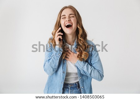 Attractive happy young girl standing isolated over white background, talking on mobile phone