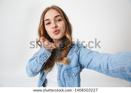 Attractive excited young girl standing isolated over white background, taking a selfie, sending kiss
