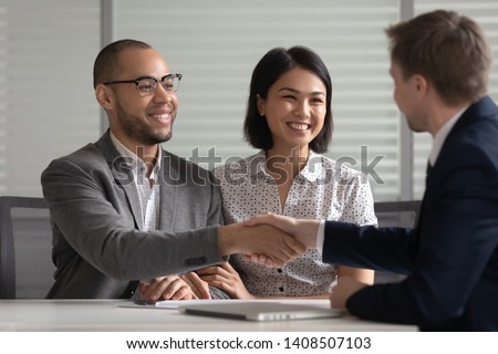 Happy mixed ethnicity young family couple clients customers handshake bank manager agent make agreement mortgage deal taking loan buying insurance investing savings shake hand of male insurer broker