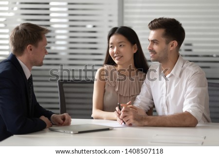 Happy mixed ethnicity couple customers talk to lawyer bank manager at meeting consulting about investment insurance real estate deal, young family clients listen to broker insurer explaining benefits