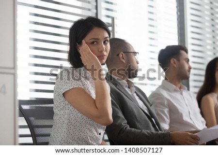 Stressed nervous inexperienced asian business woman feeling headache afraid scared worried before performance sitting on chair among diverse applicants in row queue room waiting for job interview Royalty-Free Stock Photo #1408507127