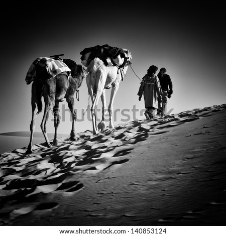 square black & white image of 2 men and 2 camels in Sahara desert