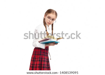 Side view of unhappy nerdy girl in school uniform and glasses looking at camera while reading textbook against white background