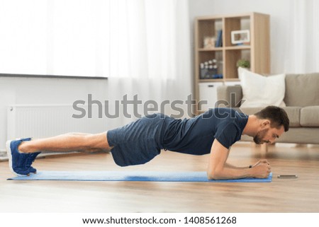 sport, fitness and healthy lifestyle concept - man looking at smartphone and doing plank exercise at home Royalty-Free Stock Photo #1408561268