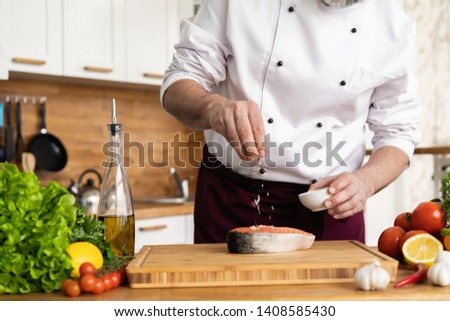 The chef prepares fresh fish salmon, trout, sprinkles with sea salt and vegetables. Horizontal photo. Concept cooking healthy and vegan cuisine, clean food, restaurants, hotel business