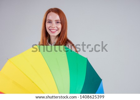 beautiful redhead girl on a white background in the style striped shirt with rainbow an umbrella. autumn fashion look seasonal spring sale
