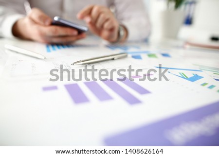 Businessman hold smartphone aganist silver pen with business chart background. Financial statistic family budget concept.