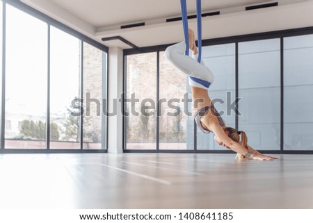 Young woman practicing Aerial yoga exercise or antigravity yoga in light yogi class or studio with large beautiful windows. Pilates, stretch, balance, healthy lifestyle people. Anti-gravity