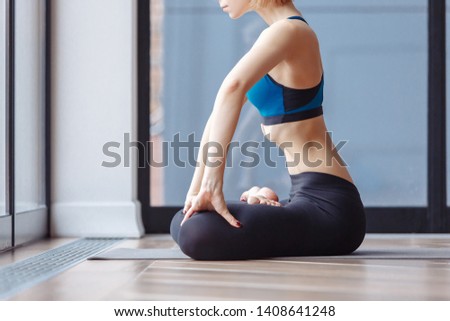 Young woman in white gymnastic suit makes vacuum exercise for muscles internal organs of abdomen sitting on floor at home. Padmasana, Lotus Posture, performing Upward Abdominal Lock, Uddiyana Bandha