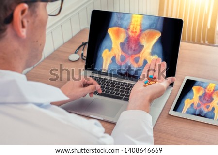 Doctor holding pills with x-ray of hips and spine with pain on a laptop. Digital tablet on the desk