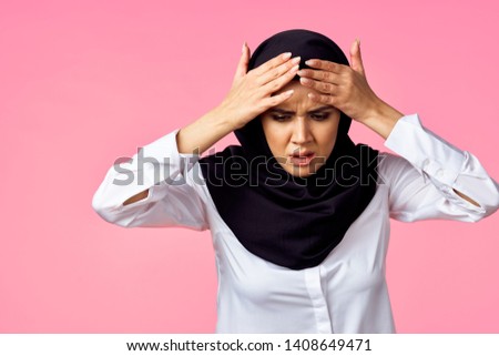  woman in a black burqa with a headache on a pink background                              