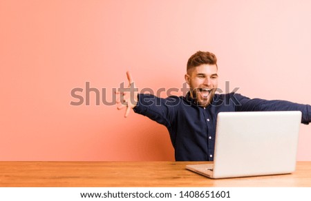 Young man working with his laptop feels confident giving a hug to the camera.