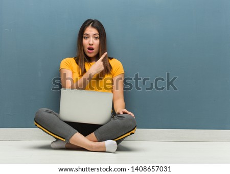 Young woman sitting on the floor with a laptop pointing to the side
