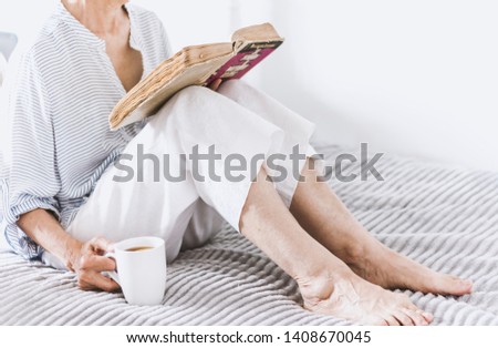 Old woman on the bed reading old book with cup of lemon tea