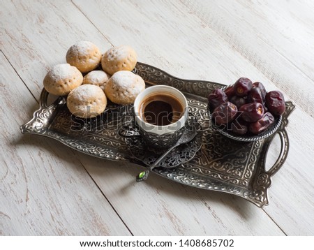 Top view on silver plate with sweets, date fruits and coffee cup on the white wooden table. Ramadan background.