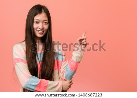 Young cool chinese woman smiling cheerfully pointing with forefinger away.