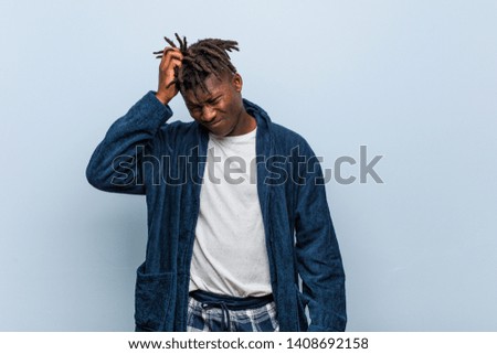 Young african black man wearing pajama tired and very sleepy keeping hand on his head.