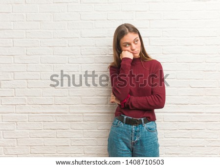 Young cool woman over a bricks wall thinking of something, looking to the side