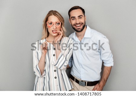 Photo closeup of positive couple in casual clothing laughing and holding paper fake glasses on stick isolated over gray wall