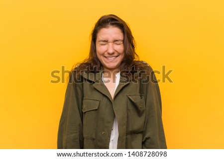 Young european woman isolated over yellow background laughs and closes eyes, feels relaxed and happy.