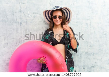 Young european woman holding a inflatable donut smiling and raising thumb up